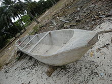 An angled view of a wooden boat lying on the sand with some trees in the background