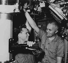 Two men, Petty Officer Edward Carbullido and Captain Edward L. Beach (left to right), standing next to the periscope in the conning tower compartment of the nuclear submarine USS Triton