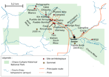 A large green area representing Chaco Culture National Historical Park's boundaries sits in the middle of a white field. The green area is roughly rectangular with one smaller square-like and one triangular appendage abutting it at bottom-left and bottom-right, respectively. Fifteen small red circles represent the location of important Chacoan sites; they are focused on a line running from top-left (northwest) to bottom-right (southeast). A dashed blue line depicting the Chaco Wash runs roughly along the same line; a network of dashed and solid orange lines represent trails and metalled roads, respectively, also focus on the same axis, connecting the red dots. Two gold squares define high points: "Fajada Butte (2019 m.)" and "West Mesa (2035 m.)".