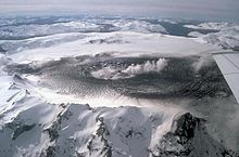 Glaciers around a black caldera from which steam is rising