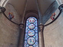  A semi-circular area with stone walls, a domed ceiling and a tall stained glass window with prominent circular decorations.