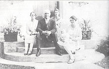 A man and three women seated on the front stoop of a house. One of the women is cradling a baby.