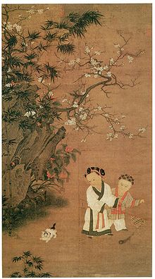 Two young girls play with a toy consisting of a long feather attached to a stick, while a cat watches them. There is a large rock formation and a flowering tree to the left of the girls and the cat.