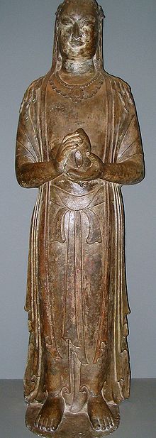 A standing Buddha: a yellow statue made from limestone, with its hands in prayer and holding a lotus