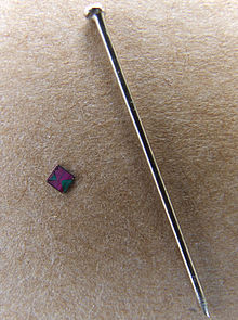 Photo of computer chip beside sewing pin, which is over 10 times the length of the chip.