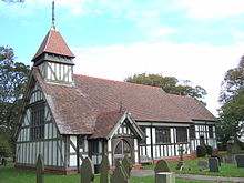 A small black and white half-timbered church showing the nave with a porch, a small chancel beyond and a small spire on the nearside of the roof; some gravestones visible in the churchyard.
