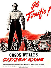 On a white background, the centre of the poster is dominated by a stern looking man in a white shirt and black trousers towering over a group of people. "It's terrific!" appears in red in italics in the top right of the picture tipped 60° to the right. "Orson Welles" appears in block letters below the group of people and the man in the white suit. "Citizen Kane" appears in red italics below that. The remaining credits are listed in fine print in the bottom of the picture.