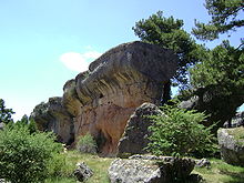 One of Ciudad Encantada's rock formations: The top of this wall of stone is rounded and wider than its base; sparse forestation surrounds the formation.