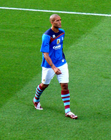 A man wearing a blue t-shirt and white shorts standing on a grass field