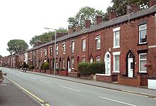 View down a street of two-storey brick-built terraced houses.