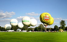 Several white balloons and two yellow balloons taking off from a grassy field