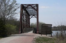 Through truss bridge with wooden-decked walkway; bench beside trail