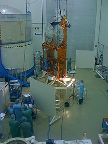 A group of people looking at a gold spacecraft on a stand in the middle of a room