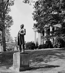 sculpture of man on grass with mansion and trees