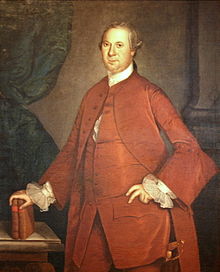 An eighteenth century painting shows a middle aged man dressed in red clothing leaning on two books that are resting on a table, with a Roman-style column in the background