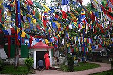 A man and a woman praying at a small white shrine dedicated to Lord Ganesh. Several colourful flags on buntings are strung across poles in front of the shrine.