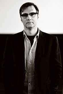 A man wearing glasses, a jacket and an open necked shirt