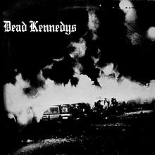 A black-and-white photograph of a burning car outdoors at night. In the upper-left corner are the words "Dead Kennedys" in Gothic script.