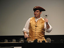 Man wearing tricorn hat and vest ringing a glass handbell