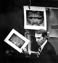 Souviron is seen in the courtroom. Several enlargements of dental x-rays have been pinned up, and he is holding one in his hand.