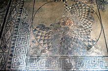 An ancient mosaic depicting the gorgon Medusa in the centre of a round geometric shield inscribed into a square also decorated with geometric motifs