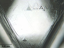 A triangular facet of a crystal having triangular etch pits with the largest having a base length of about 0.2 mm
