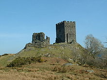 upon a grassy hillock stands two rectangular built fortifications. The one to the left is ruinous while the one to the right appears whole with battlements