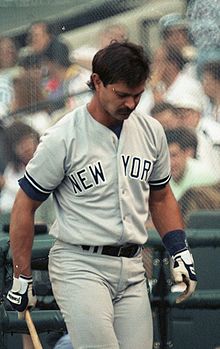 Don Mattingly wearing a gray baseball uniform holds a baseball bat with his left arm.