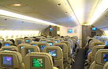Airline economy cabin. Rows of seats arranged between two aisles. Each seatback has a monitor.