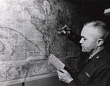 A balding man holding a small card titled "Ship's Position" writes a black line on a map of the Earth.