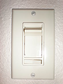  Vertical rectangular plastic cover plate with vertically sliding knob and a smaller horizontal rocker switch below. Two exposed slotted screw heads hold the cover plate to the wall box.