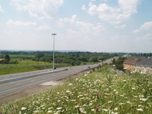 A freeway changes into a four lanes conventional road, and vanishes into the rural foothills