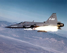 Gray jet fighter aircraft fires a white missile.