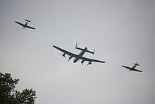 Rear view of a three-aircraft flypast. In the middle is a four-engine bomber, which is flanked on both sides by propeller-driven fighters.