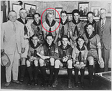 Two men in suits and another man in a boy scout uniform stand beside 10 seated teenaged boys in Boy Scout uniforms. Ford is indicated by a red circle.