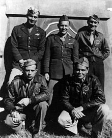 A monochrome photograph of five men wearing military pilot uniforms, three standing, two squatting, in front of a decorative Chinese structure