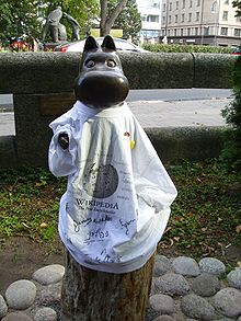 A dark metallic statue of a cartoon hippopotamus wearing a white t-shirt with the Wikipedia logo and signatures in various languages.