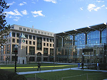 Two modern glass and concrete building side by side in front of an open grass lawn which has a short clocktower on the left side.