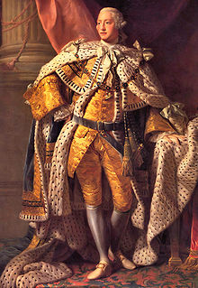 Full-length portrait in oils of a clean-shaven young man in eighteenth century dress: gold jacket and breeches, ermine cloak, powdered wig, white stockings, and buckled shoes.