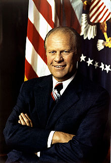 President Gerald Ford, arms folded, in front of a United States Flag and the Presidential seal.