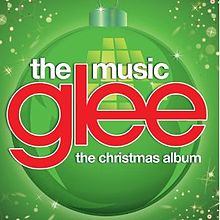 The word "Glee" is in large lowercase red print and centered on a green background with a Christmas bauble. Beneath it are the words "The Christmas Album" and above are "The Music", both in lowercase white font.