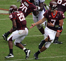 A quarterback hands off the football to his running back. The team is dressed in Chicago maroon and burnt orange jerseys with white pants.