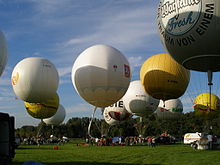 Many white and yellow gas balloons taking off from a grassy field