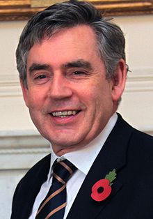 Head and shoulders of a smiling man in a suit and striped tie with dark, greying hair and rounded face with square jaw
