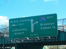 A green sign on an overpass reading Grand Central Parkway east LaGuardia Airport left straight on left three lanes I-278 west Brooklyn Staten Island right lane exit 1/2 mile