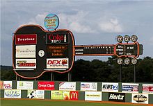 A view of the giant black guitar-shaped scoreboard beyond the left-center field wall. Advertisements for local businesses adorn the guitar and the green outfield wall below.