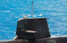 Close-up of the submarine's fin. Two naval officers, a small flag, and the periscope mast are on top of the fin.