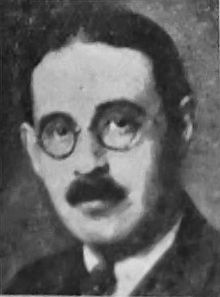 Black and white portrait photo of a white male with dark hair, glasses and a mustache