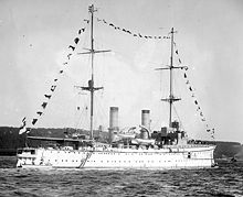 Black-and-white photograph of white ship with tall masts travelling on water.