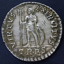Silver coin showing a man standing with a standard and a round shield behind his legs. There is writing round the edge including "TRPR" below the figure.